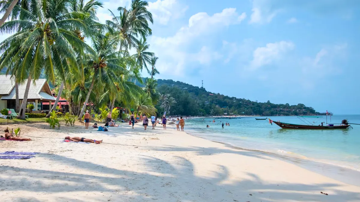 Haad Yao on Koh Phangan’s west coast Tropical beach with palm trees, people relaxing, and a boat on calm blue water